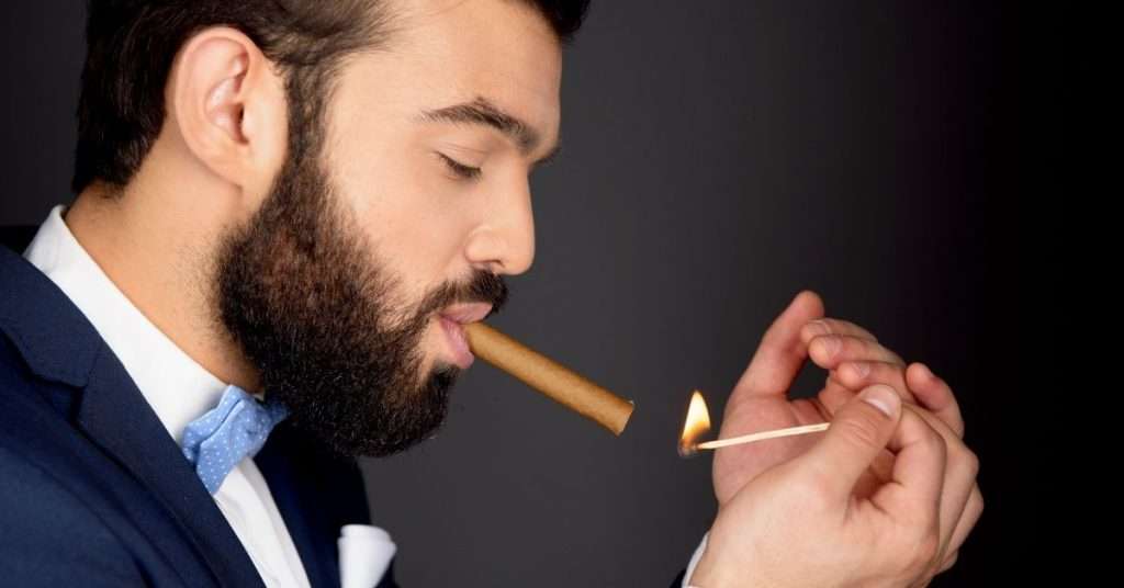 bearded man lighting a cigar